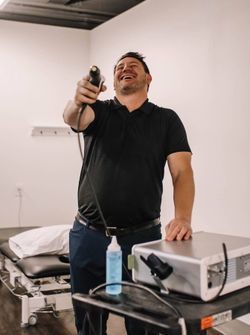 Adam Giesbrecht laughing while holding a shockwave therapy gun.