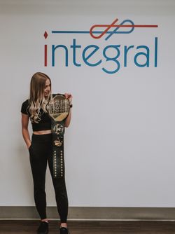 Kaitlyn Sosnowski standing in front of the Integral logo with the graduation belt over her shoulder.